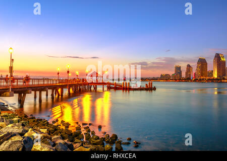 Malerischer Blick auf Coronado Anlegestelle der Fähre auf die Insel Coronado, Kalifornien, USA. Die Innenstadt von San Diego in der Dämmerung auf den Hintergrund. Alte hölzerne Pier widerspiegelt Stockfoto