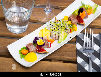 Teller mit leckeren gebratenen Thunfisch mit Mango, Avocado und Feigen auf lange Platte serviert. Stockfoto