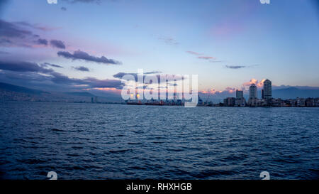 Stadtbild der Stadt Izmir, Türkei, aus der Ägäis. Blick auf die Wolkenkratzer und der Kaufmann Port während der Dämmerung. Sonnenuntergang spiegelt sich in der Stockfoto