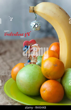 Eine Platte mit einer Banane, Mandarinen, und grüne Äpfel auf den Sack. Miniatur Paar in der Liebe. Glücklich gruss Valentinstag Karte Stockfoto