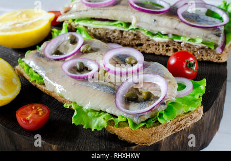Sandwich mit Gesalzener Hering, Butter und roten Zwiebeln auf alten rustikalen Schneidebrett. Selektiver Fokus Stockfoto