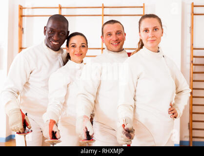 Gruppe positiver Fechter stehen mit Folien zusammen an fechten Training Stockfoto