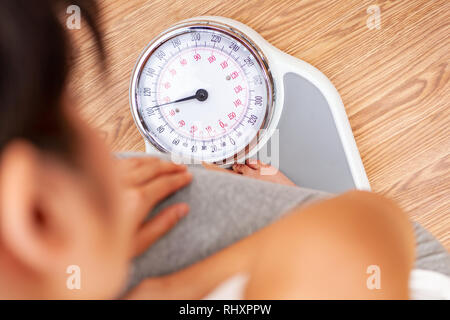 Weibliche junge Frau steht auf einer Waage zu Hause oder im Fitnessstudio Stockfoto