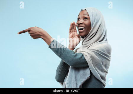 Geheimnis, Klatsch-Konzept. Junge afrikanische Frau flüstert ein Geheimnis hinter ihrer Hand. Die Frau isoliert am trendigen Blau studio Hintergrund. Junge emotionale Frau. Menschliche Gefühle, Mimik Konzept. Stockfoto