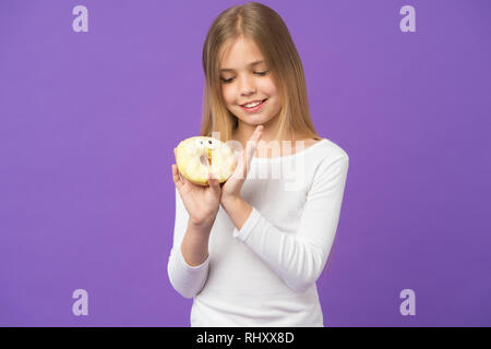 Mädchen auf lächelnde Gesicht hält süßen Donut in der Hand, violett unterlegt. Sweet Tooth Konzept. Mädchen, die an Krapfen mit Paar Augen. Junge Mädchen mit langen Haaren gerne Süßigkeiten und Leckereien. Stockfoto
