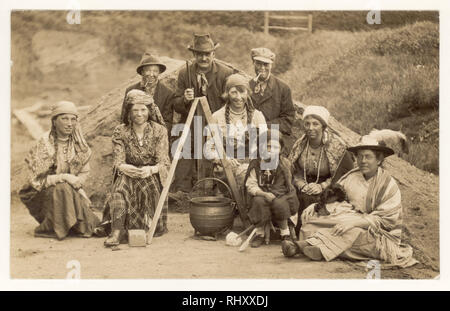 Anfang 1900 Postkarte von Familie als Zigeuner in traditioneller Kleidung, geschwärzte Gesichter, stitting Neben Kochtopf, für ein Gruppenfoto posieren gekleidet, Großbritannien ca. 1920 Stockfoto