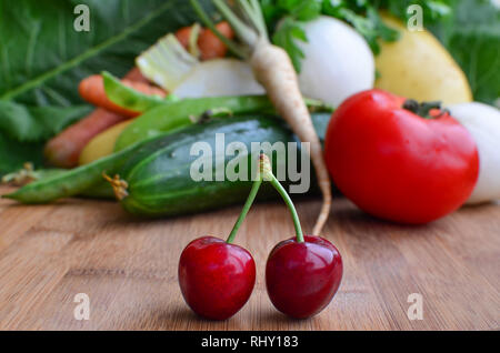 Bambus Schneidebrett voller Vitamine, ein paar frische, reife Kirschen im Vordergrund und viele verschiedene Art von Gemüse im Hintergrund Stockfoto