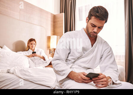 Leben in Smartphones. Paare sind mit Smartphones im Hotel Zimmer Bett. Technologien gewinnen Stockfoto