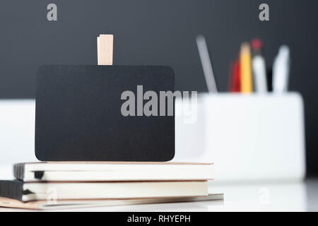 Close up Clip Blackboard auf Notebook mit blur modernen Pencil Box auf dem Tisch und dunkelgraue Wand im Büro Schreibtisch, Mock, um Platz für die Anzeige des Designs oder Te Stockfoto