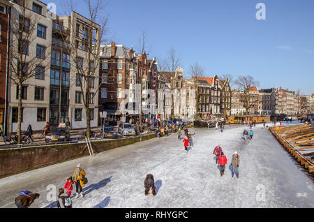 Die Menschen genießen einen kalten sonnigen Tag Wandern und Eislaufen auf einem zugefrorenen Kanal in Amsterdam, Niederlande. Stockfoto