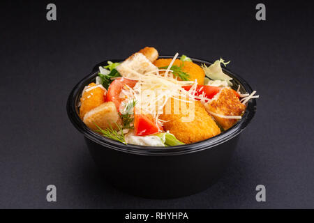 Salat mit gebratenen Hähnchenstreifen, Cracker und Parmesan auf Schwarz bacground Stockfoto