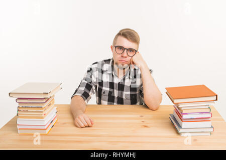 Schüler, die Untersuchung und die Bildung Konzept - Müde junge Mann am Tisch sitzen mit Bergen von Büchern Stockfoto