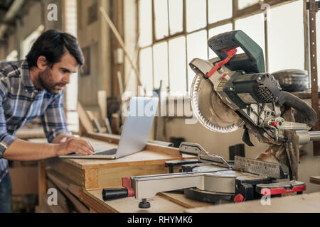 Carpenter stützte sich auf eine Werkbank voller Tools online arbeiten Stockfoto