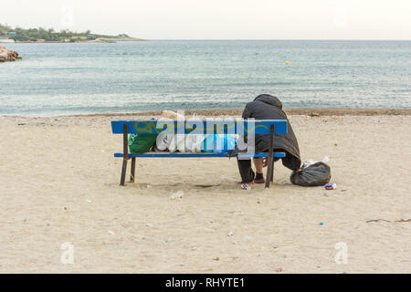 Obdachlose Frau ist allein auf einer Bank sitzen an der Küste mit ihrem Material in Taschen, ohne Hoffnung, Meer, Sandstrand Stockfoto