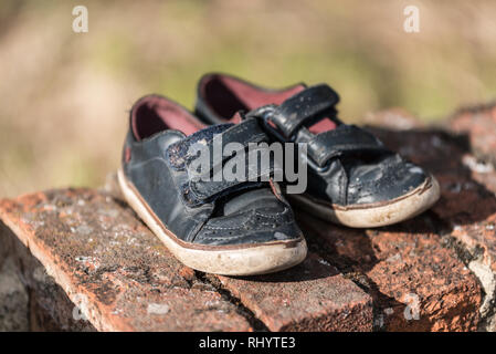 Ein paar verloren, verlassenen Kind Schuhe können Symbol einige fehlende Kind, ein paar kid Schuhe auf eine Mauer aus Stein Stockfoto