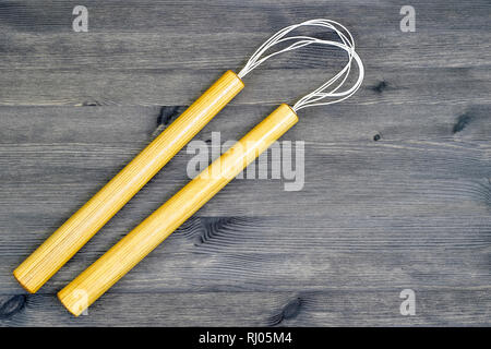 Ein paar Holz- nunchucks aus Asche auf einem grauen Hintergrund aus Holz im Landhausstil. Stockfoto