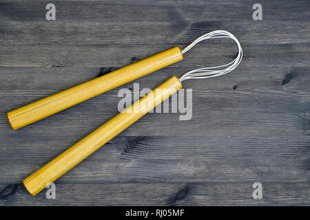 Ein paar Holz- nunchucks aus Asche auf einem grauen Hintergrund aus Holz im Landhausstil. Stockfoto