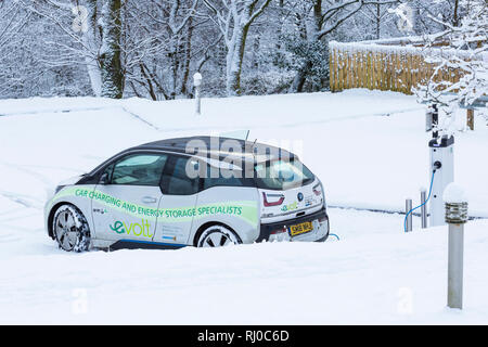 BMW-Elektroauto an elektrischen Auto aufgeladen Ladestation Punkt in verschneiten Parkplatz durch Clachaig Inn, Glencoe, Highlands, Schottland im Winter Stockfoto