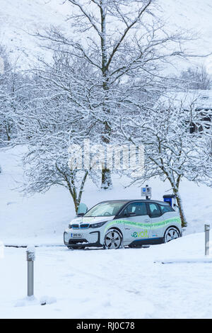 BMW-Elektroauto an elektrischen Auto aufgeladen Ladestation Punkt in verschneiten Parkplatz durch Clachaig Inn, Glencoe, Highlands, Schottland im Winter Stockfoto