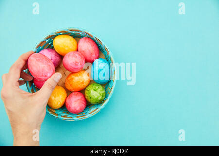 Hand mit einem bunten Ostereier über Korb an Ostern Stockfoto