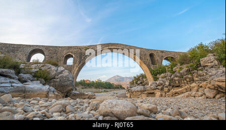 Die mesi Brücke (Ura e Mesit) in Mes, Albanien, in der Nähe von Shkodra. Ein alter Stein osmanische Brücke - die größte im Land. Trockenen Fluss und die Berge Stockfoto