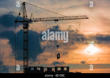 Silhouette von Turmdrehkranen und unvollendete multi-stöckiges Gebäude im Bau in den Strahlen der untergehenden Sonne der schönen Sonnenuntergang Stockfoto