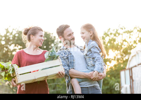 Glückliche Familie mit Gemüse in der Kiste sprechen auf der Farm gegen Sky Stockfoto