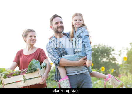Glückliche Familie mit Gemüse in der Kiste auf der Farm gegen Sky Stockfoto