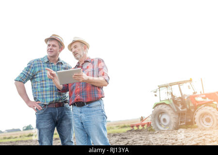 Landwirte mit digitalen Tablet diskutieren auf dem Feld gegen den Himmel in der Farm Stockfoto