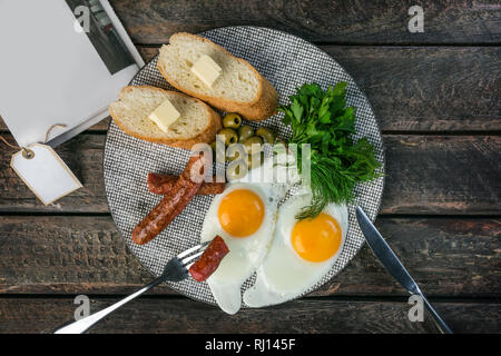 Leckeres Frühstück. Rührei mit Oliven und gegrillte Würstchen. Von Besteck serviert mit Brot und Butter. Zeitung mit Platz für Ihren Text. Top Stockfoto