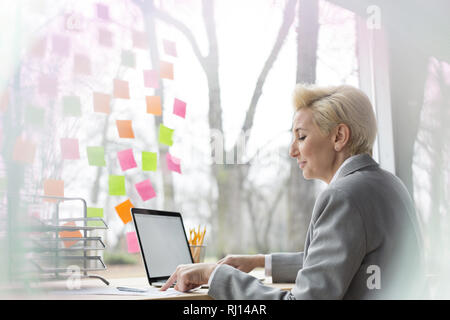 Im mittleren Alter blonde Frau an Ihren Laptop an ihrem Schreibtisch arbeiten im Büro Stockfoto