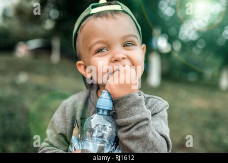 Kleiner Junge Kind 3-5 Jahre, Nahaufnahme Porträt, glücklich, in seinen Händen hält eine Flasche Wasser zu lachen. Im Sommer in der Stadt an der frischen Luft Stockfoto