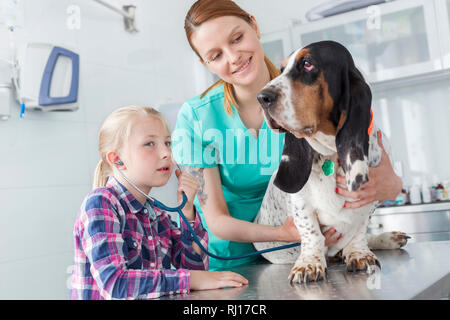 Tierärztin mit Hund am Tisch, während Mädchen hören durch Stethoskop an der Klinik Stockfoto