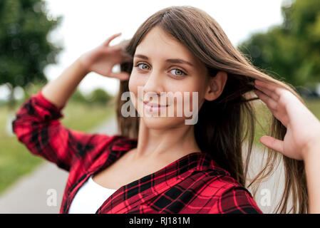 Schöne Mädchen mit langen Haaren Jugendlicher 11-12 Jahre alt, im Sommer in der City Park. Glücklich lächelnde, glättet das Haar. Close-up Smart Look Stockfoto