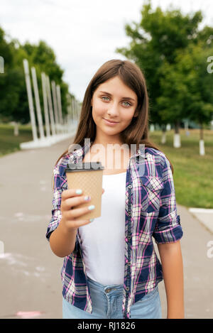 Schöne Mädchen Teenager 11-12 Jahre alt, im Sommer City Park stehen. Glücklich lächelt, hält ihre Hand bei einer Tasse Kaffee oder Tee. Konzept eines Angebots Stockfoto