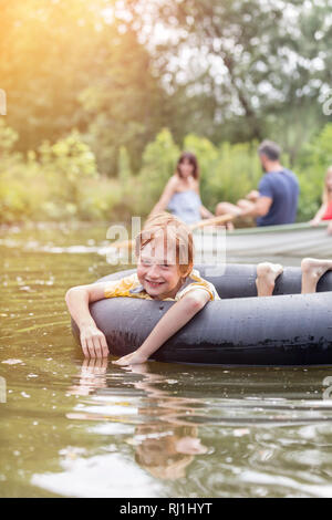 Portrait von lächelnden Jungen floating mit aufblasbaren Ring gegen Familie Bootfahren in See Stockfoto
