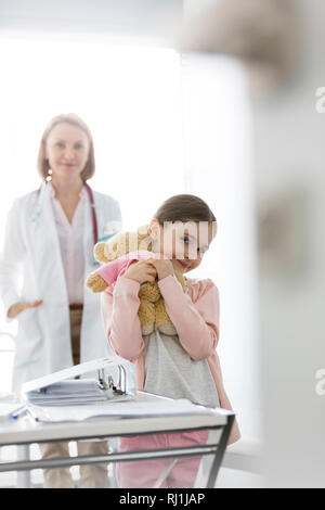 Portrait von lächelnden Mädchen mit Teddybär stehend gegen Arzt am Krankenhaus Stockfoto