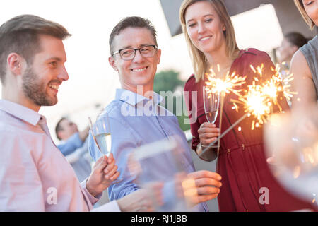 Lächelnd Kollegen holding Wunderkerzen und Weingläser während der Party auf dem Dach Stockfoto