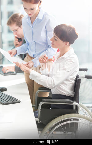 Behinderte Unternehmerin diskutieren über Dokument mit Kollegen am Schreibtisch in modernen Büro Stockfoto