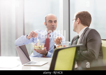 Unternehmer im Gespräch mit Kollegen, während das Mittagessen im Sitzungssaal während der Sitzung im Büro Stockfoto