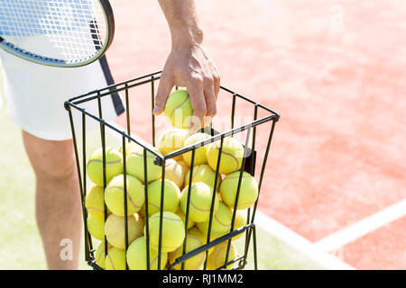 Mittelteil des Menschen Kommissionierung Tennis ball von metallischen Korb an einem sonnigen Tag Stockfoto