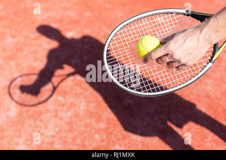 7/8 Hand von reifer Mann mit tennisball auf dem roten Hof bei sonnigen Tag Stockfoto