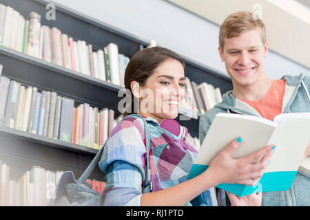 Lächelnd Freunde buch Kommunikation gegen Regal an der Universität Bibliothek Stockfoto