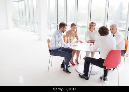 Kollegen diskutieren beim Sitzen am Tisch durch die Fenster im neuen Büro Stockfoto