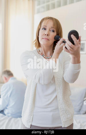 Reife Frau Anwendung Make-up beim Stehen im Schlafzimmer Stockfoto