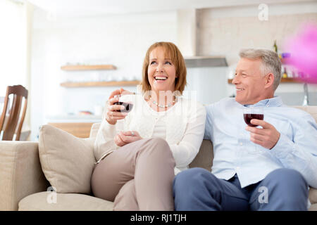 Lächelnd reifes Paar sitzt auf dem Sofa, während sie Getränke zu Hause Stockfoto