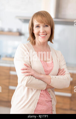 Portrait von lächelnden reife Frau, die mit Waffen zu Hause gekreuzt Stockfoto
