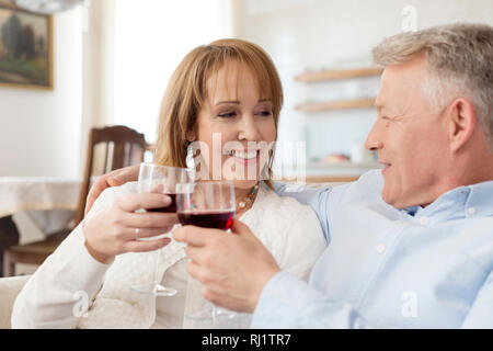 Lächelnd reifes Paar toasten Weingläser, während auf dem Sofa zu Hause sitzen Stockfoto