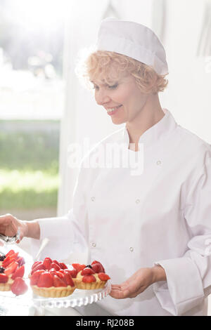 Lächelnd reifen Chef arrangieren frische Erdbeere Torten im Restaurant Stockfoto