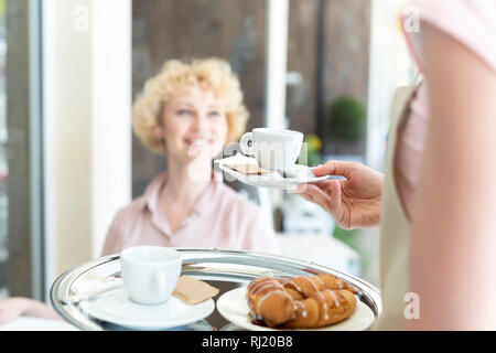 Mittelteil der jungen Kellnerin serviert Espresso zu lächeln reife Kunden im Restaurant Stockfoto